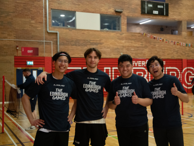 Four participants stand together in an indoor sports hall, posing for a group photo while wearing matching navy T-shirts with the text “The Edinburgh Games.
